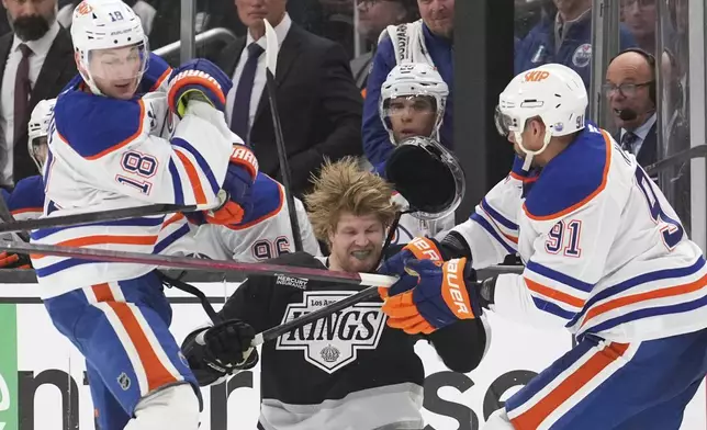 Los Angeles Kings left wing Warren Foegele, center loses his helmet as he is hit by Edmonton Oilers left wing Zach Hyman, left, and left wing Evander Kane during the second period in Game 2 of an NHL hockey first-round playoff series Wednesday, April 23, 2025, in Los Angeles. (AP Photo/Mark J. Terrill)