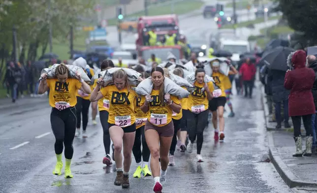 Women's race competitors, including winner Ferne Gardner, front, No. 11, run with a 20kg sack of coal over a 1.1km course during the World Coal Carrying Championships in Ossett, West Yorkshire, England, on Monday, April 21, 2025. (AP Photo/Jon Super)