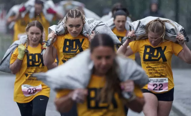 Women's race competitors, including Jodie Ounsley, center, who plays Fury in the British TV show "Gladiators," run with a 20kg sack of coal over a 1.1km course during the World Coal Carrying Championships in Ossett, West Yorkshire, England, Monday, April 21, 2025. (AP Photo/Jon Super)