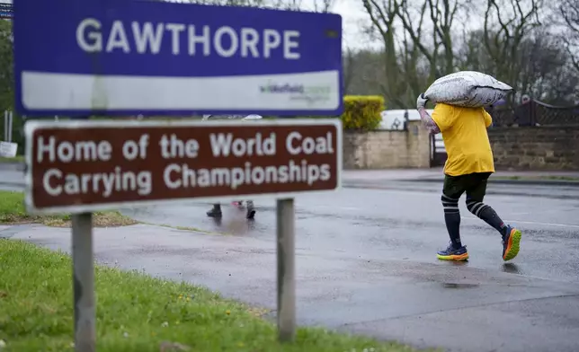 A contestant carrying a 50kg sack of coal passes a road sign at the World Coal Carrying Championships in Ossett, West Yorkshire, England, Monday, April 21, 2025. (AP Photo/Jon Super)