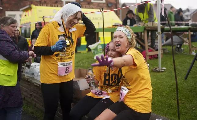 Women's race contestants react at the finish after running with 20kg sacks of coal over a 1.1 km course during the World Coal Carrying Championships in Ossett, West Yorkshire, England, Monday, April 21, 2025. (AP Photo/Jon Super)