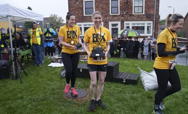Verity Rees from Windermere, Florida, center, holds her trophy after winning the women's open category at the World Coal Carrying Championships in Ossett, West Yorkshire, England, Monday, April 21, 2025. (AP Photo/Jon Super)