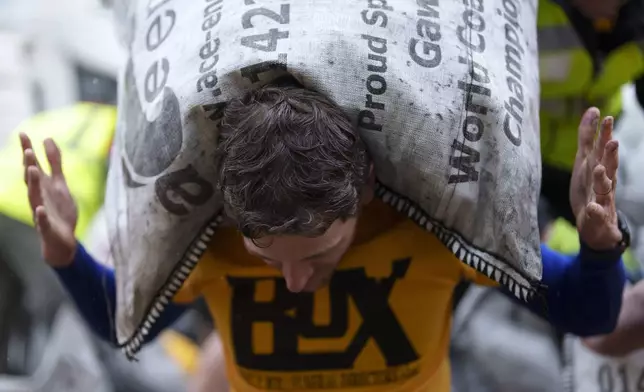 A contestant loads a 50kg bag of coal onto his shoulders during the World Coal Carrying Championships in Ossett, West Yorkshire, England, Monday, April 21, 2025. (AP Photo/Jon Super)