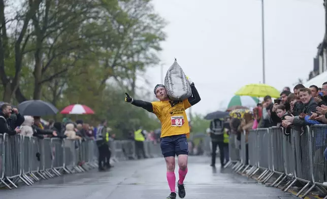 Brett Spencer gestures to the crowd as he makes his way to the finish line carrying a 50kg sack of coal during the World Coal Carrying Championships in Ossett, West Yorkshire, England, Monday, April 21, 2025. (AP Photo/Jon Super)