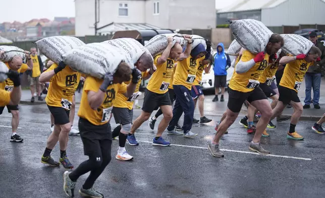 Contestants take off from the start line carrying 50kg sacks of coal along a 1.1km course at the World Coal Carrying Championships in Ossett, West Yorkshire, England, Monday, April 21, 2025. (AP Photo/Jon Super)