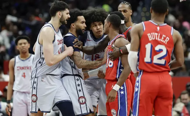 Washington Wizards forward Kyshawn George, center, is held back by teammates after being fouled by Philadelphia 76ers guard Lonnie Walker IV, right, during the first half of an NBA basketball game in Washington, Wednesday, April 9, 2025. (AP Photo/Terrance Williams)