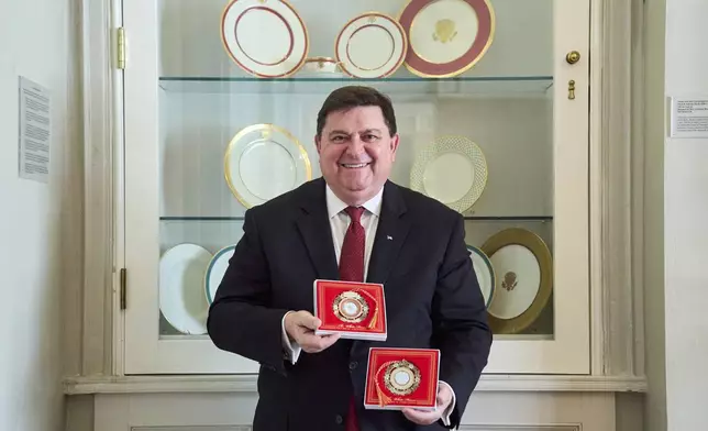 White House Historical Association President Stewart McLaurin poses with the 2025 White House Christmas ornament, seen both front and back, in front of a display of White House china, Thursday, April 10, 2025, at the association in Washington. (AP Photo/Jacquelyn Martin)