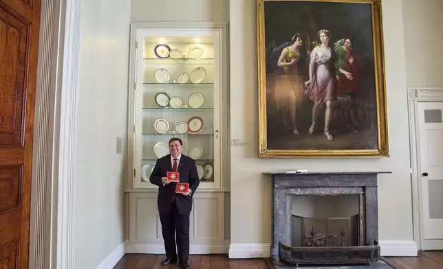 White House Historical Association President Stewart McLaurin poses with the 2025 White House Christmas ornament, seen both front and back, in front of a display of White House china, Thursday, April 10, 2025, at the association in Washington. (AP Photo/Jacquelyn Martin)