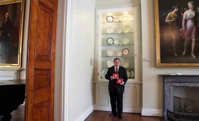 White House Historical Association President Stewart McLaurin poses with the 2025 White House Christmas ornament, seen both front and back, Thursday, April 10, 2025, at the association in Washington. (AP Photo/Jacquelyn Martin)