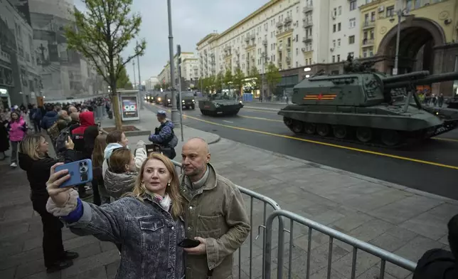 People take a selfie photo with military vehicles driving along Tverskaya street toward Red Square to attend a rehearsal for the Victory Day military parade in Moscow, Russia, on Tuesday, April 29, 2025. (AP Photo/Pavel Bednyakov)
