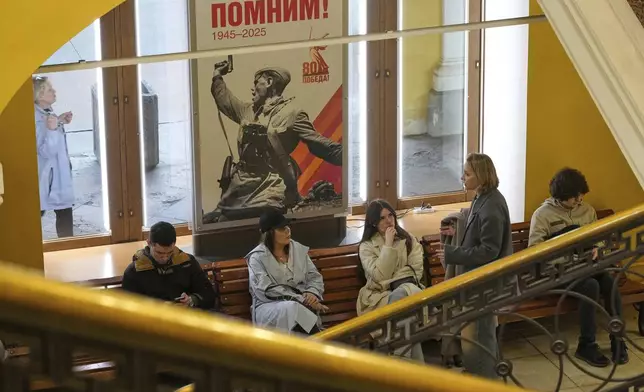 People sit in a shop next to a poster showing the photograph Kombat (a battalion commander) by Soviet photographer Max Alpert depicting a Soviet officer armed with a TT pistol during World War II, ahead of celebrations of the 80th anniversary of the Soviet Union's victory over Nazi Germany during the World War II, in St. Petersburg, Russia, Tuesday, April 29, 2025. (AP Photo/Dmitri Lovetsky)