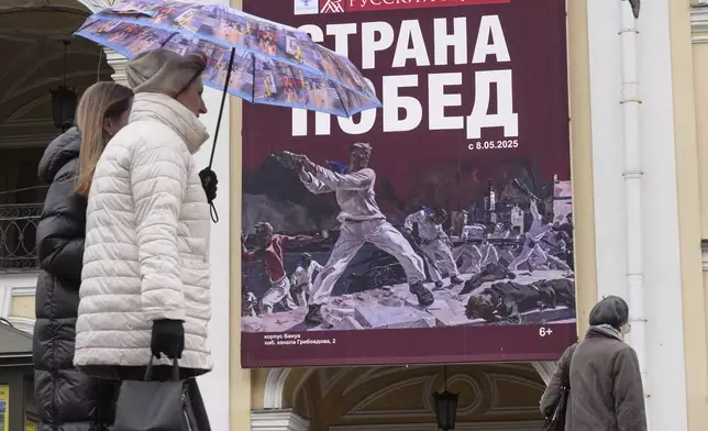 People walk past a poster featuring the painting "The Defense of Sevastopol" by Soviet painter Aleksandr Deyneka and words reading "The country of victories" ahead of celebrations of the 80th anniversary of the Soviet Union's victory over Nazi Germany during the World War II, in St. Petersburg, Russia, Tuesday, April 29, 2025. (AP Photo/Dmitri Lovetsky)