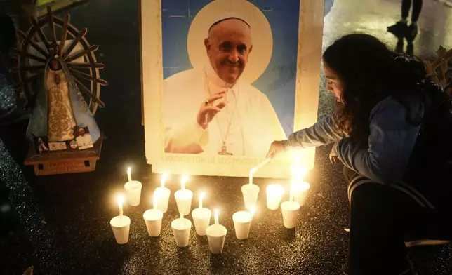 A mourner lights a candle in front of a picture of the late Pope Francis outside the Cathedral in Buenos Aires, Argentina, Saturday, April 26, 2025, as his funeral takes place in Rome. (AP Photo/Natacha Pisarenko)