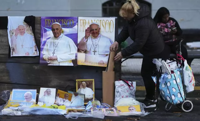 A street seller stands next to posters of the late Pope Francis outside the Cathedral in Buenos Aires, Argentina, Saturday, April 26, 2025, as his funeral takes place in Rome. (AP Photo/Natacha Pisarenko)