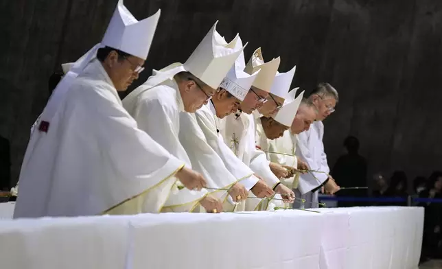 The Most Rev. Archbishop Francisco Escalante Molina, third left, Auxiliary Bishop Andrea Lembo, fourth left, and other priests lay flowers on a table installed near a portrait of the late Pope Francis at the end of a memorial Mass at St. Mary's Cathedral in Tokyo, Sunday, April 27, 2025. (AP Photo/Hiro Komae, Pool)