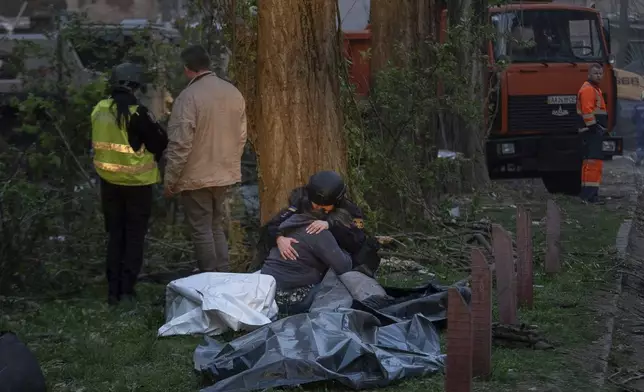 A rescue psychotherapist hugs a woman who lost a loved one, in front of the bodies of victims after a Russian strike in a residential neighborhood in Kyiv, Ukraine, Thursday, April 24, 2025. (AP Photo/Alex Babenko)