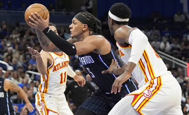 Orlando Magic forward Paolo Banchero (5) drives between Atlanta Hawks guard Trae Young (11) and forward Onyeka Okongwu, right, during the second half of an NBA basketball game, Tuesday, April 8, 2025, in Orlando, Fla. (AP Photo/John Raoux)