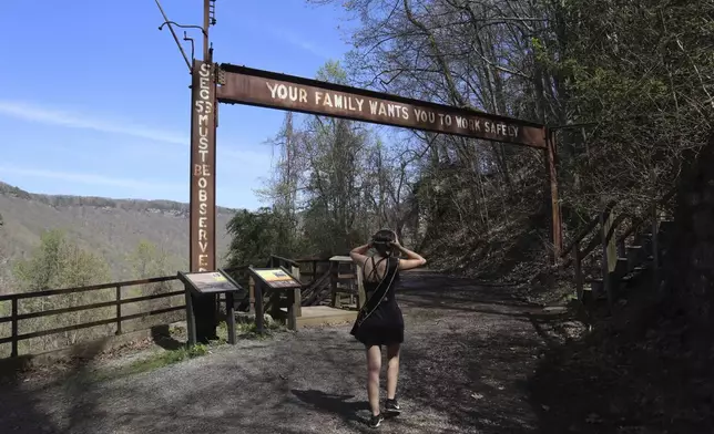 West Virginia Coal Festival teen beauty pageant winner Ava Johnson, 16, walks under a sign urging miners to work safely at the former Kay Moor coal town and camp in the New River Gorge National Park and Preserve near Fayetteville, W.Va., Thursday, April 17, 2025, (AP Photo/Leah Willingham)
