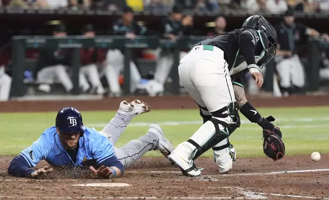 Tampa Bay Rays' Danny Jansen, left, scores a run as Arizona Diamondbacks catcher Jose Herrera, right, reaches for the ball on a late throw during the seventh inning of a baseball game Wednesday, April 23, 2025, in Phoenix. (AP Photo/Ross D. Franklin)