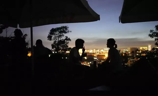 People sit on the terrace of a closed bar at the Monte Agudo viewpoint overlooking Lisbon during a nationwide power outage, Monday, April 28, 2025. (AP Photo/Armando Franca)