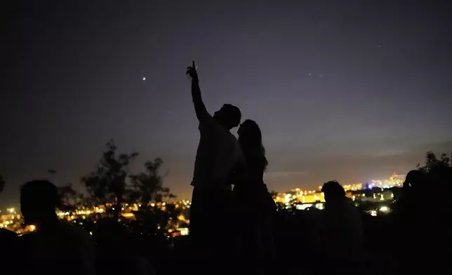A young couple stands on a wall looking at the sky at a viewpoint overlooking Lisbon during a nationwide power outage, Monday, April 28, 2025. (AP Photo/Armando Franca)