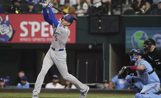 Los Angeles Dodgers' Freddie Freeman (5) follows through on a sacrifice fly that allowed Will Smith to score as Texas Rangers catcher Jonah Heim and umpire Nic Lentz, right, look on in the eighth inning of a baseball game in Arlington, Texas, Sunday, April 20, 2025. (AP Photo/Tony Gutierrez)