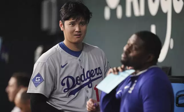 Los Angeles Dodgers' Shohei Ohtani talks with a staff member in the dugout in the seventh inning of a baseball game against the Texas Rangers in Arlington, Texas, Sunday, April 20, 2025. (AP Photo/Tony Gutierrez)