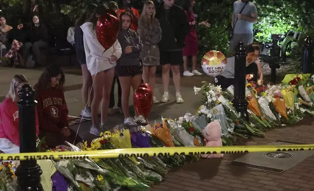 An impromptu memorial shared online brings students bearing flowers into the evening near the center of the Florida State campus in sight of the Student Union building, Tallahassee, Fla., Thursday, April 17, 2025. (AP Photo/Gary McCullough)