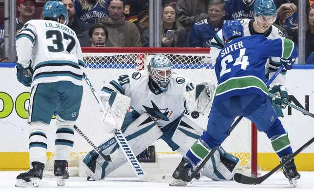 San Jose Sharks goaltender Alexandar Georgiev (40) stops Vancouver Canucks' Pius Suter (24) as Sharks' Timothy Liljegren (37) and Henry Thrun (3) watch during the first period of an NHL hockey game in Vancouver, British Columbia, Monday, April 14, 2025. (Ethan Cairns/The Canadian Press via AP)