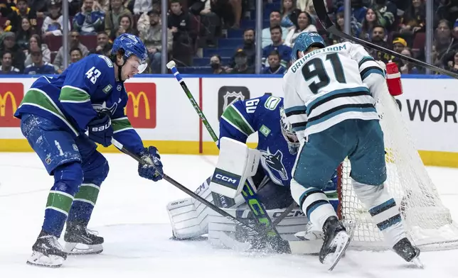 Vancouver Canucks goaltender Nikita Tolopilo (60) prepares to stop San Jose Sharks' Carl Grundstrom (91) as Canucks' Quinn Hughes (43) watch during the first period of an NHL hockey game in Vancouver, British Columbia, Monday, April 14, 2025. (Ethan Cairns/The Canadian Press via AP)