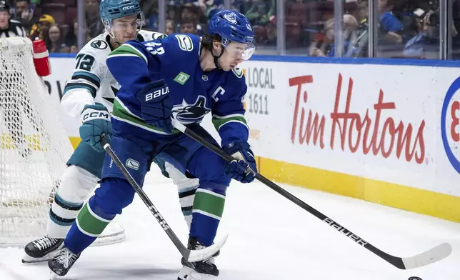 San Jose Sharks' William Eklund (72) and Vancouver Canucks' Quinn Hughes (43) vie for the puck during the first period of an NHL hockey game in Vancouver, British Columbia, Monday, April 14, 2025. (Ethan Cairns/The Canadian Press via AP)
