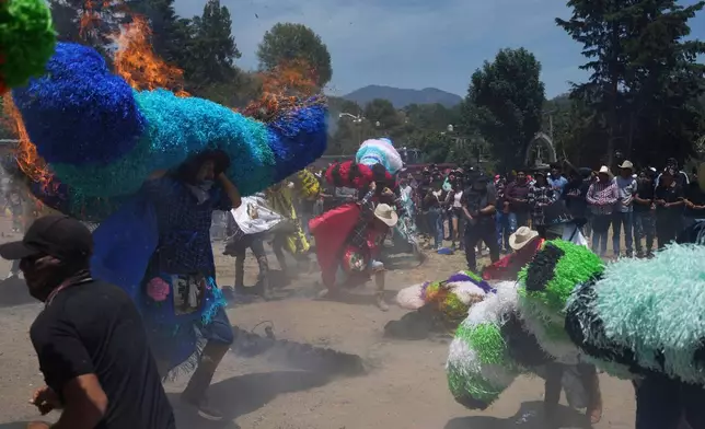 Revelers, known as a sayones, try to put out fires they started on tissue paper hats as part of Easter celebrations in Tetela del Volcan, Mexico, Sunday, April 20, 2025. (AP Photo/Eduardo Verdugo)