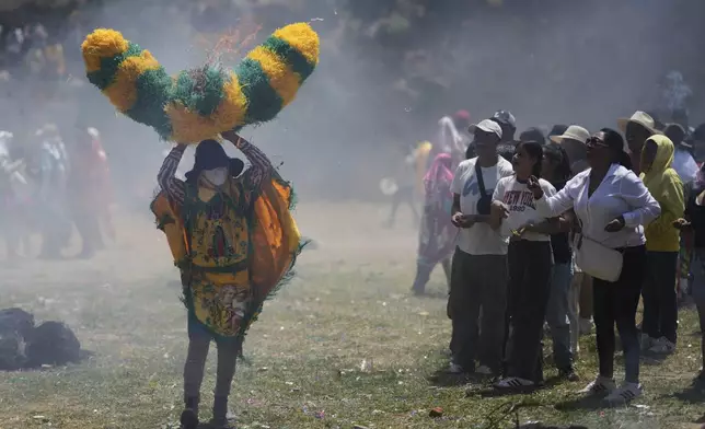 Onlookers throw lit matches at a reveler, known as a sayon, wielding a tissue paper hat during Easter celebrations in Tetela del Volcan, Mexico, Sunday, April 20, 2025. (AP Photo/Eduardo Verdugo)