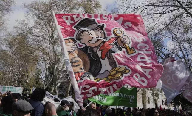 People march with a flag depicting a rich banker during a demonstration to protest high housing costs in Madrid, Spain, Saturday April 5, 2025. (AP Photo/Paul White)