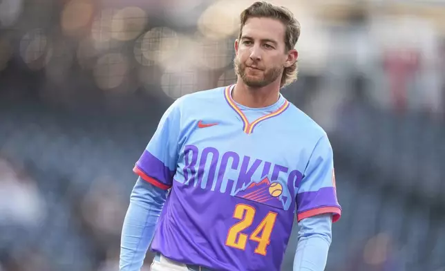 Wearing the team's new "City Connect" uniform, Colorado Rockies third baseman Ryan McMahon waits for his glove and hat after the first inning of Game 2 of a split baseball doubleheader against the Washington Nationals, Sunday, April 20, 2025, in Denver. (AP Photo/David Zalubowski)