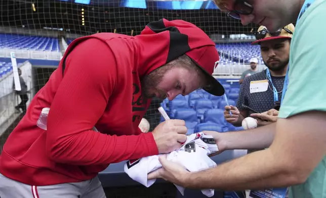 Cincinnati Reds' Gavin Lux, left, gives autographs before a baseball game against the Miami Marlins, Monday, April 21, 2025, in Miami. (AP Photo/Lynne Sladky)