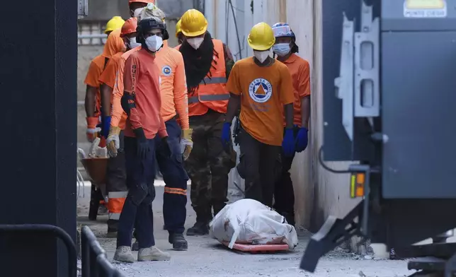 Rescue workers stand next to a recovered body of a victim who died when the roof collapsed two nights prior at the Jet Set nightclub during a merengue concert, in Santo Domingo, Dominican Republic, Wednesday, April 9, 2025, (AP Photo/Ricardo Hernandez)