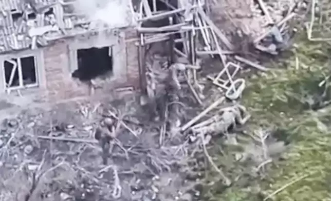 This image taken from video that European military officials say was filmed by a Ukrainian drone in the southern Ukrainian village of Piatykhatky on March 13, 2025, shows a soldier, left, identified as Russian, pointing his gun at a Ukrainian soldier who appears to be surrendering after emerging from the ruins of a house to join other Ukrainian prisoners on the ground. (Ukraine Military/European Defense Officials via AP)
