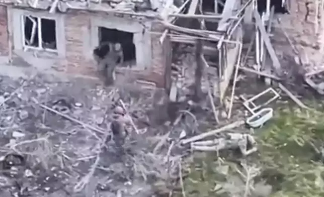 This image taken from video that European military officials say was filmed by a Ukrainian drone in the southern Ukrainian village of Piatykhatky on March 13, 2025, shows a soldier, center, identified as Russian, pointing his gun at a Ukrainian soldier who appears to be surrendering after emerging from the ruins of a house to join other Ukrainian prisoners on the ground. (Ukraine Military/European Defense Officials via AP)