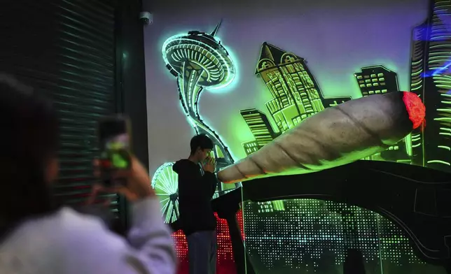 Gabriel Ramos poses for a photo in front of a large marijuana cigarette and downtown Seattle mural as Sarah Vargas takes a photo at Have a Heart cannabis dispensary Sunday, April 20, 2025, in Seattle. (AP Photo/Lindsey Wasson)