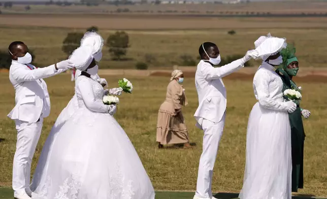 Groomsmen shield their brides from the sun as they queue during a mass Easter weddings for 3,000 people, some polygamous, at The International Pentecost Holiness Church in Heidelberg, east of Johannesburg, South Africa, Sunday, April 20, 2025. (AP Photo/Themba Hadebe)