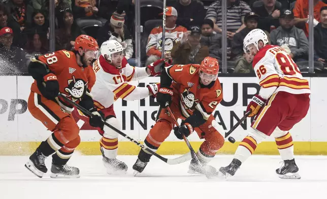 Anaheim Ducks center Isac Lundestrom, second right, shoots the puck away from Calgary Flames winger Joel Farabee, right, next to Anaheim Ducks center Jansen Harkins, left, and Calgary Flames center Yegor Sharangovich during the first period of an NHL hockey game, Wednesday, April 9, 2025, in Anaheim, Calif. (AP Photo/Etienne Laurent)