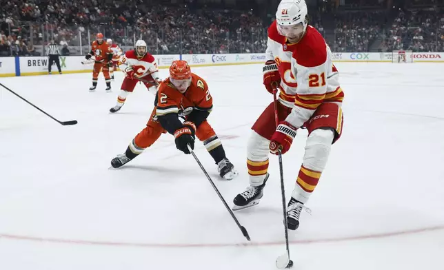 Calgary Flames center Kevin Rooney, right, controls the puck away from Anaheim Ducks defenseman Jackson LaCombe during the second period of an NHL hockey game, Wednesday, April 9, 2025, in Anaheim, Calif. (AP Photo/Etienne Laurent)