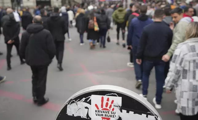 People march by a traffic sign with a sticker that reads "You have blood on your hands" ahead of a big counter-opposition protest rally planned to stage over the weekend in downtown Belgrade, Serbia, Friday, April 11, 2025. (AP Photo/Darko Vojinovic)