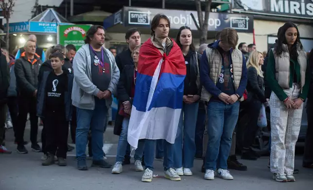 A person draped in the Serbian flag and others observe seventeen minutes of silence during an anti-corruption protest led by university students in the southwestern town of Novi Pazar, Serbia, Saturday, April 12, 2025. (AP Photo/Marko Drobnjakovic)