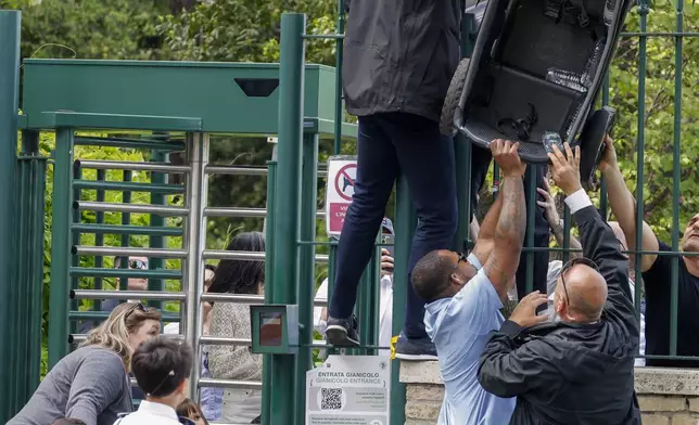 Security personnel accompanying U.S. Vice President JD Vance lift a trolley over the turnstiles at the exit of Rome's Botanic Gardens after a tour inside the gardens Vance did with his wife Usha, partially hidden behind the gate, their daughter Mirabel, sons Vivek, left, and Ewan, back to camera, Saturday, April 19, 2025. (AP Photo/Riccardo De Luca)