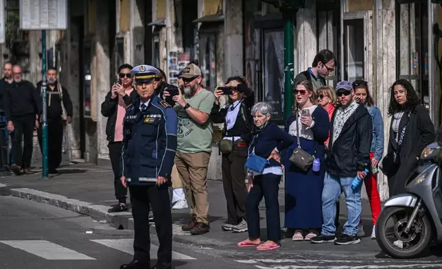 People look on as the motorcade of U.S. Vice President JD Vance passes by en route to Vatican where Vance will meet with Cardinal Pietro Parolin and Archbishop Paul Gallagher, in Rome, Italy, Saturday, April 19, 2025. (Kenny Holston/Pool Photo via AP)