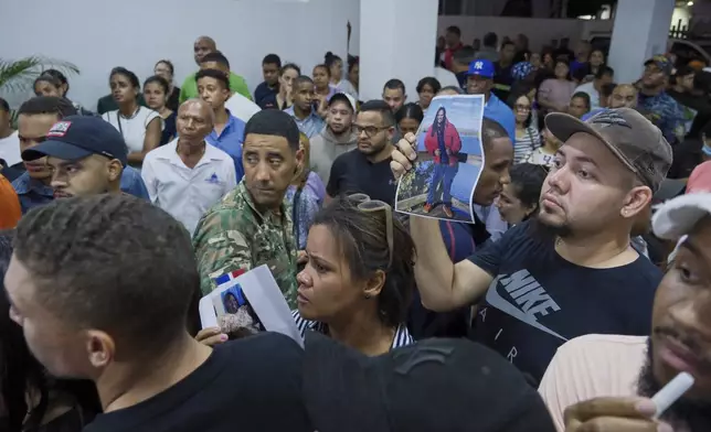 People hold up photos of their relatives while waiting to identify them at the National Institute of Forensic Pathology after the roof collapsed at Jet Set nightclub during a merengue concert in Santo Domingo, Dominican Republic, Tuesday, April 8, 2025. (AP Photo/Ricardo Hernandez)