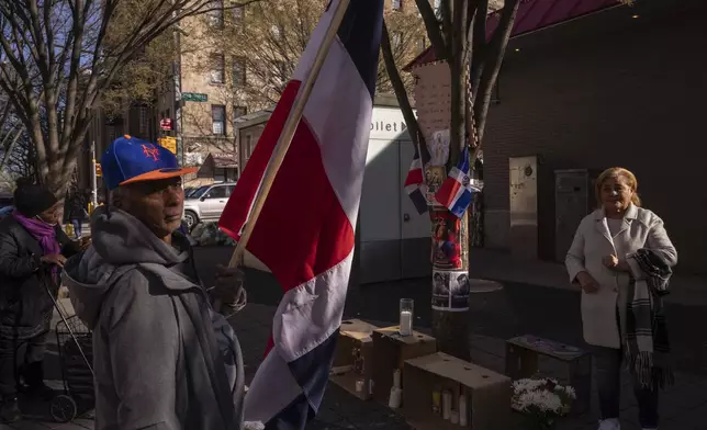 Johnny Martinez, 65, from the Dominican Republic, holds the Dominican Republic flag near a makeshift vigil for the victims of the Jet Set club roof collapse, Wednesday, April 9, 2025, in New York. (AP Photo/Adam Gray)