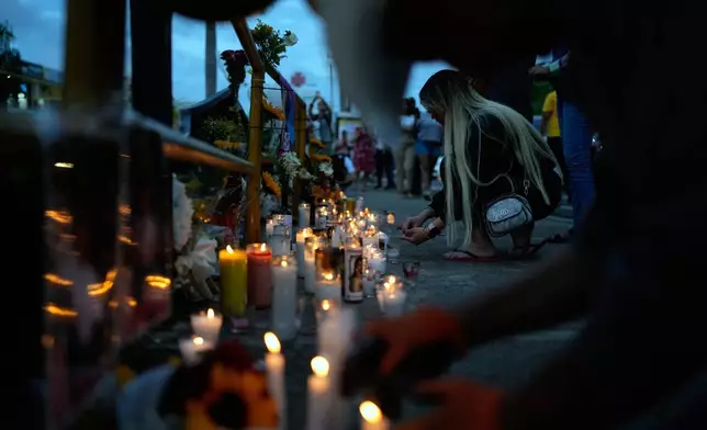 A woman lights a candle at a makeshift memorial outside the Jet Set nightclub, in memory of the more than 200 people who died when its roof collapsed, in Santo Domingo, Dominican Republic, Friday, April 11, 2025. (AP Photo/Matias Delacroix)